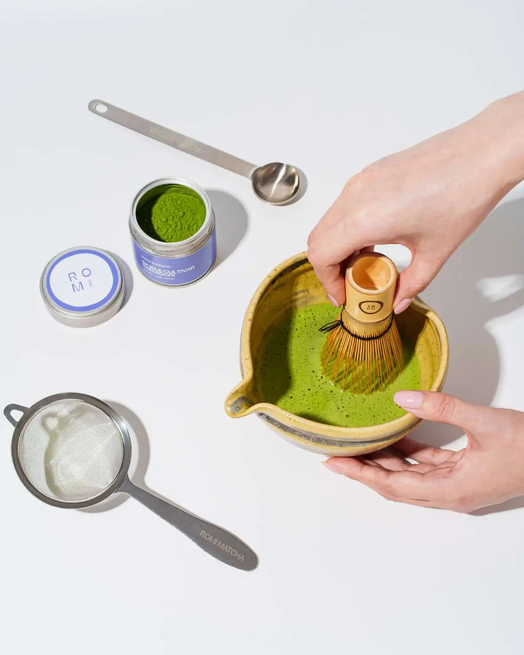 Person making matcha green tea with a whisk on a white background