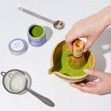 Person making matcha green tea with a whisk on a white background