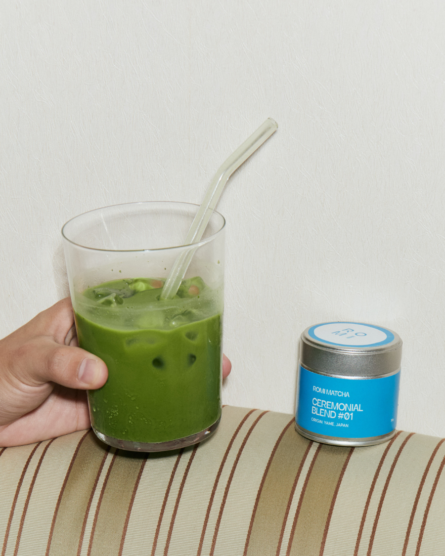 Green smoothie in a glass with a straw, next to a container of matcha powder on a striped surface.