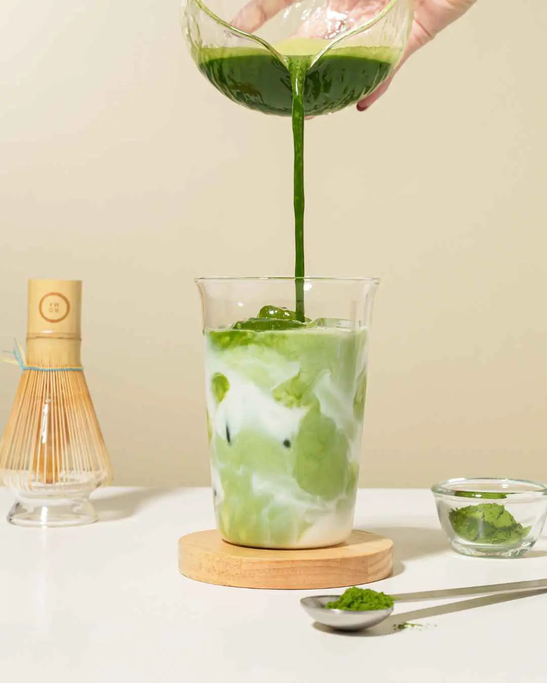 Matcha Latte pouring matcha into milk with accessories in the background