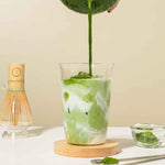 Matcha Latte pouring matcha into milk with accessories in the background