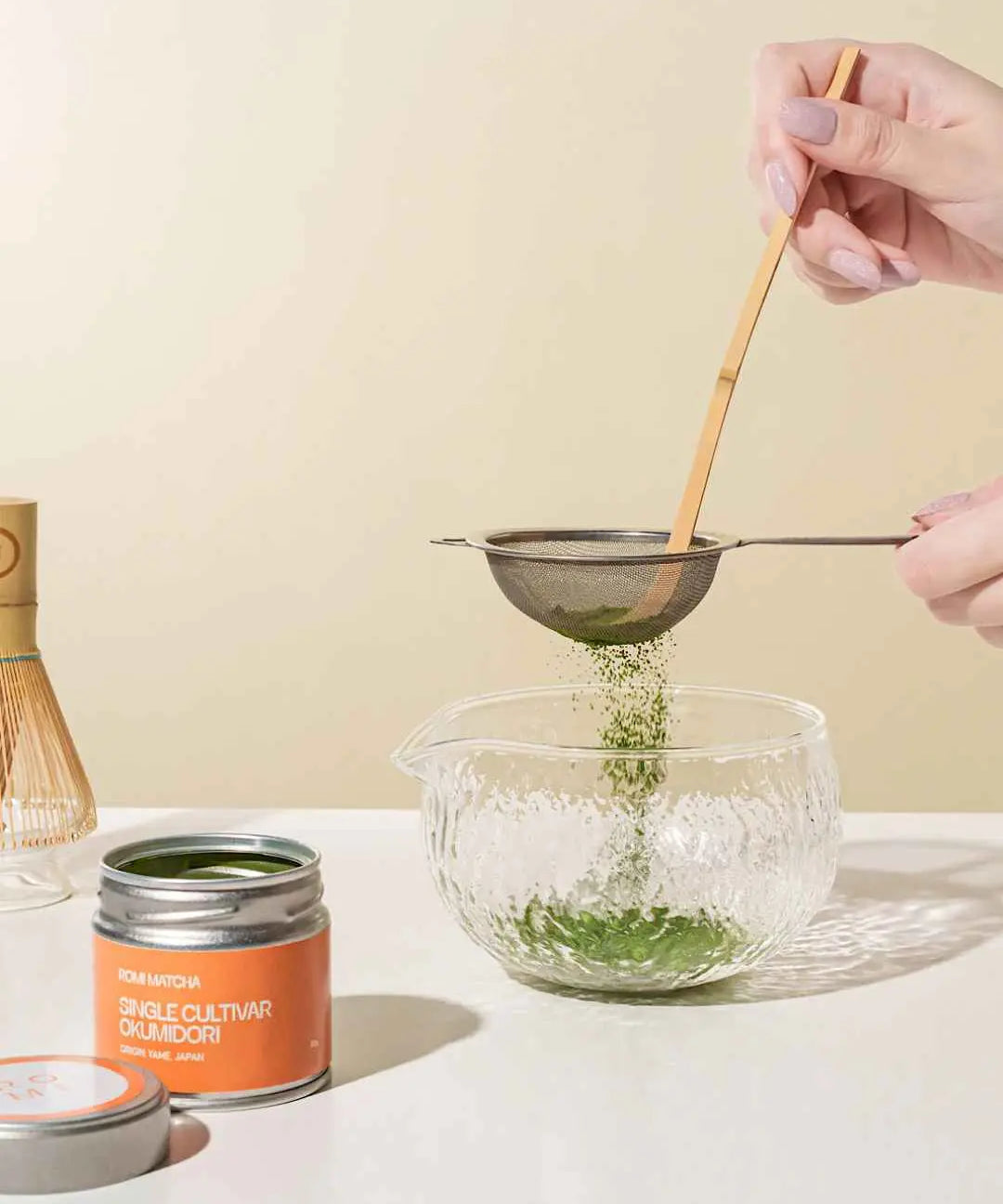 Okumidori Matcha tins with hands sifting matcha into a bowl