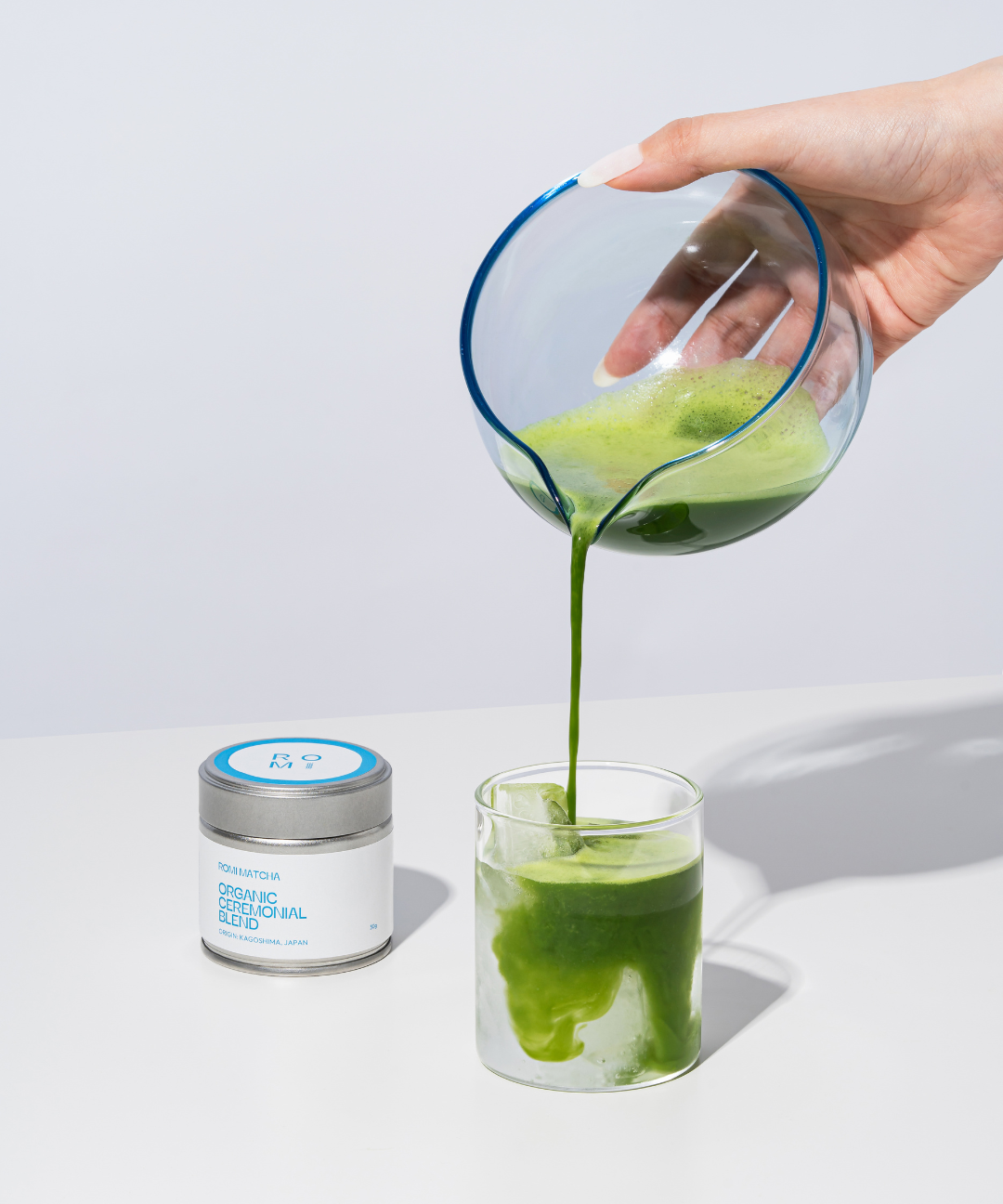 Hand pouring Romi Matcha Organic Ceremonial Blend matcha latte on white background