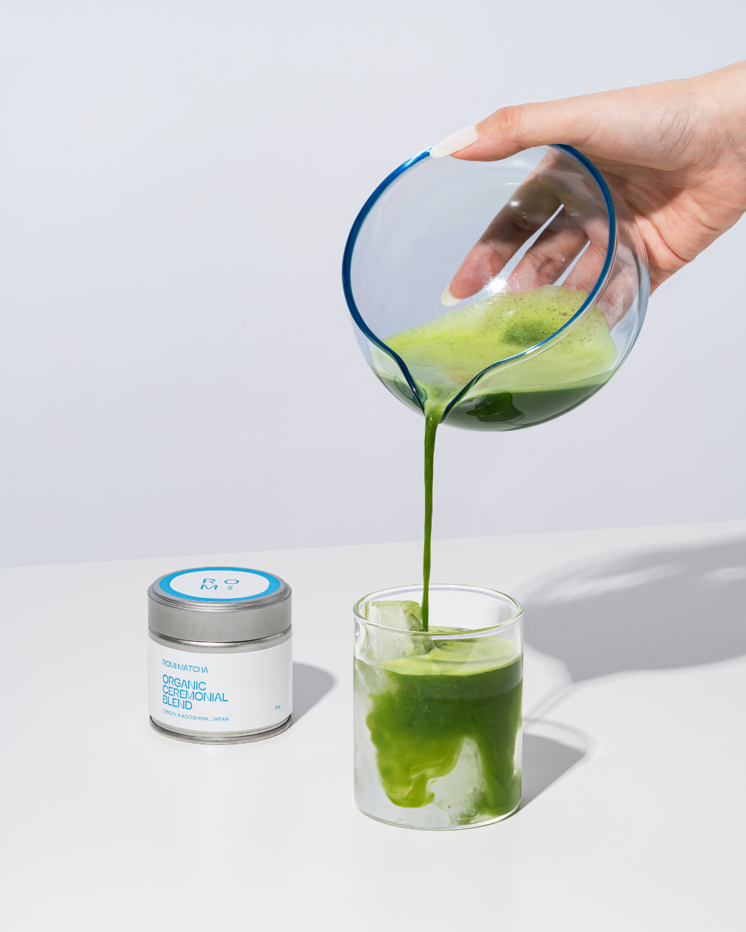 Hand pouring Romi Matcha Organic Ceremonial Blend matcha latte on white background