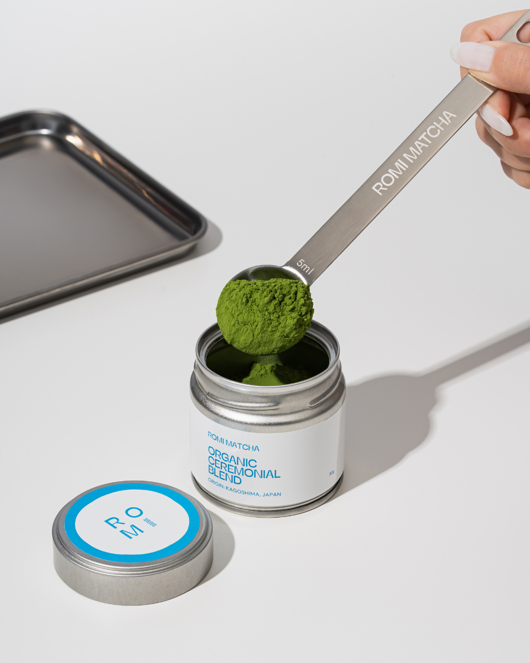 Person scooping matcha powder from a container with a spoon labeled 'ROMI MATCHA'.