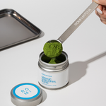 Person scooping matcha powder from a container with a spoon labeled 'ROMI MATCHA'.