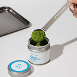 Person scooping matcha powder from a container with a spoon labeled 'ROMI MATCHA'.