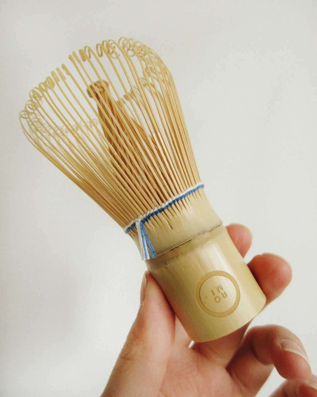 Hand holding a wooden tea whisk against a plain background