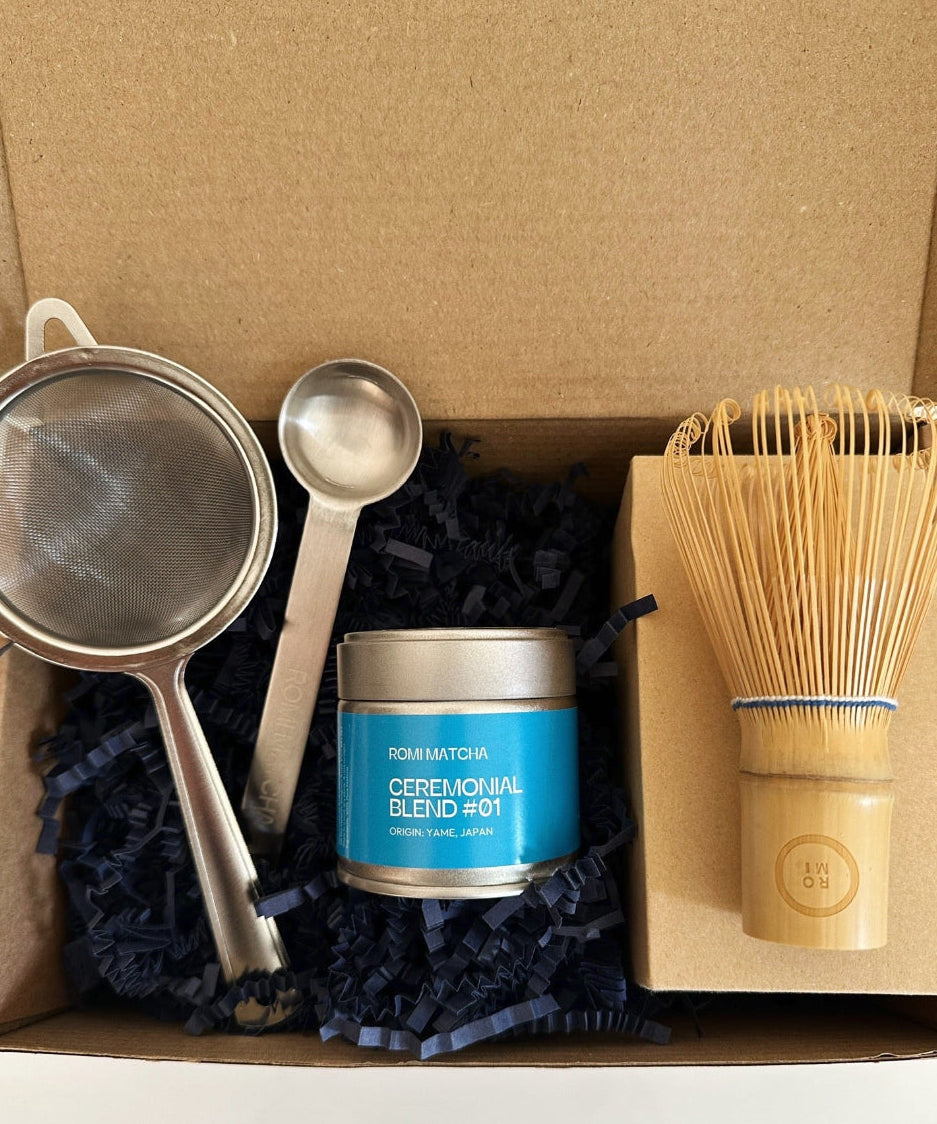 Tea-making set with a canister, strainer, spoon, and whisk in a cardboard box.