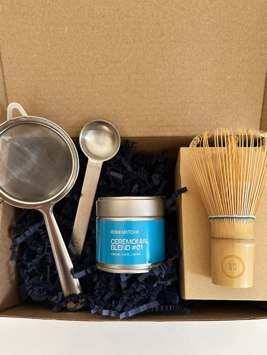 Tea-making set with a canister, strainer, spoon, and whisk in a cardboard box.