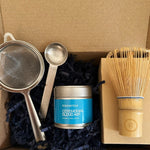 Tea-making set with a canister, strainer, spoon, and whisk in a cardboard box.