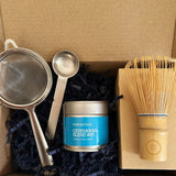 Tea-making set with a canister, strainer, spoon, and whisk in a cardboard box.