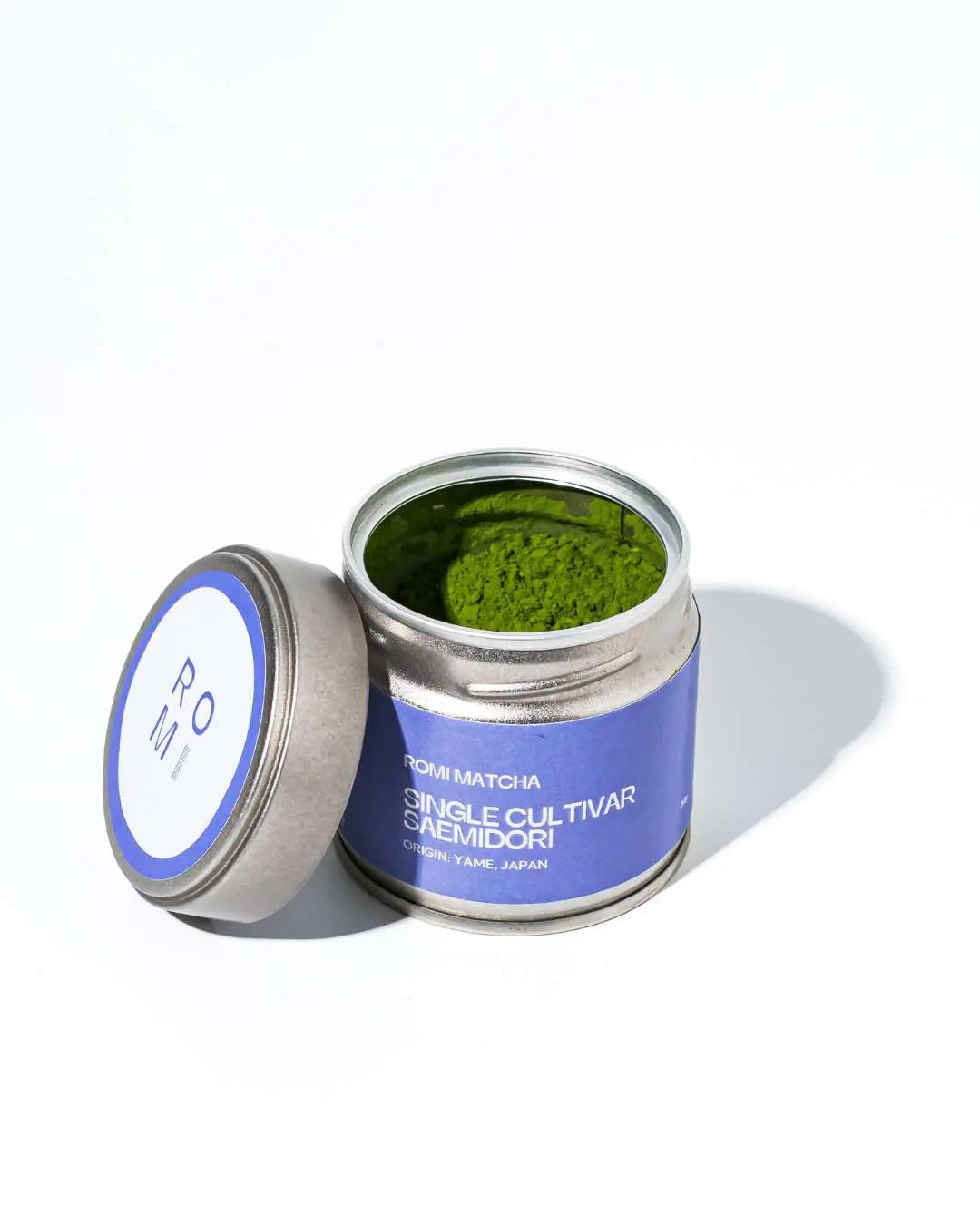 Open container of matcha green tea powder with a Romi Matcha purple label on a white background