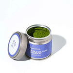 Open container of matcha green tea powder with a Romi Matcha purple label on a white background