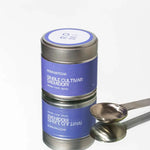 Tea canister with a purple label and silver spoon on a white background