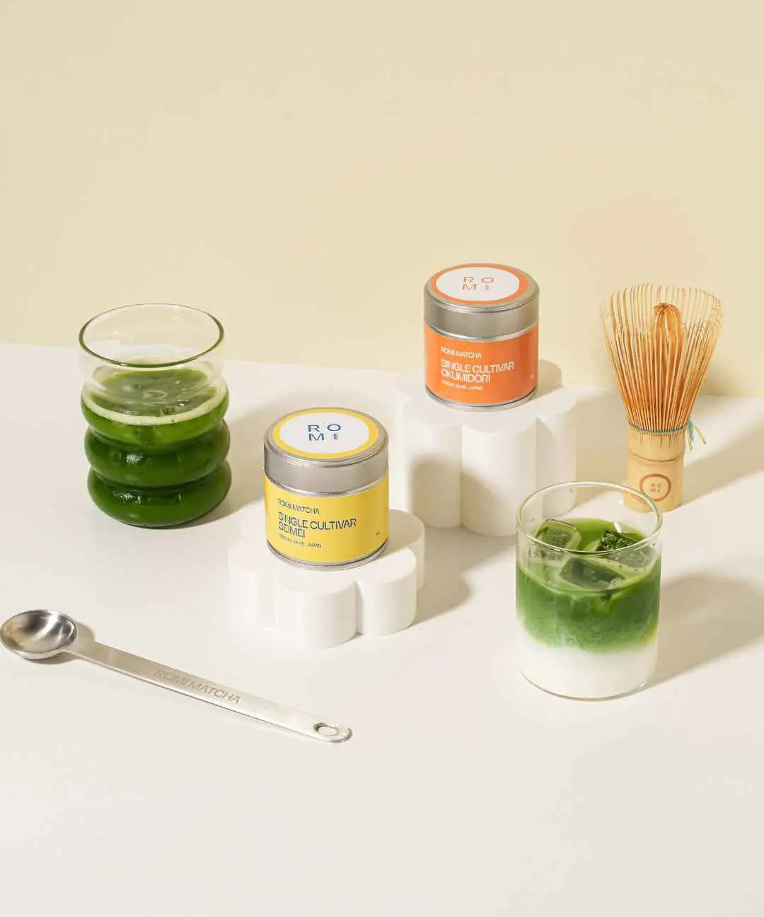 Matcha tins of single cultivars with matcha in glasses, with spoon and bamboo whisk in the background