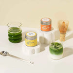 Matcha tins of single cultivars with matcha in glasses, with spoon and bamboo whisk in the background