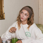 Woman sitting at a table with a green matcha latte and a white sweatshirt.
