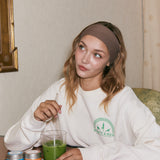 Woman sitting at a table with a green matcha latte and a white sweatshirt.