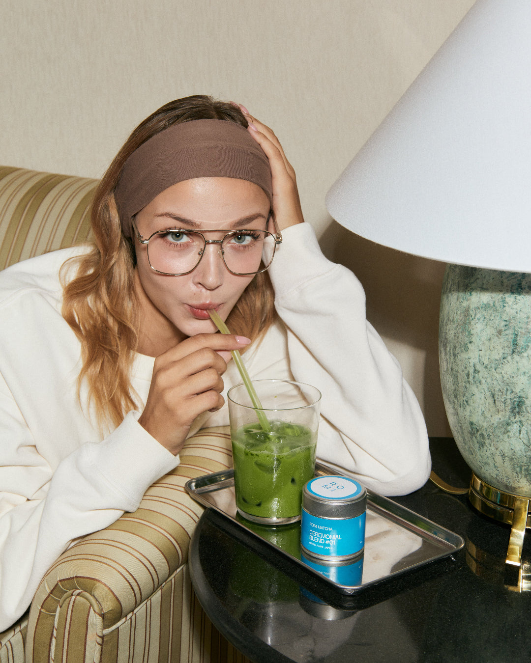 Woman drinking a green beverage with a straw in a cozy indoor setting.