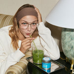 Woman drinking a green beverage with a straw in a cozy indoor setting.