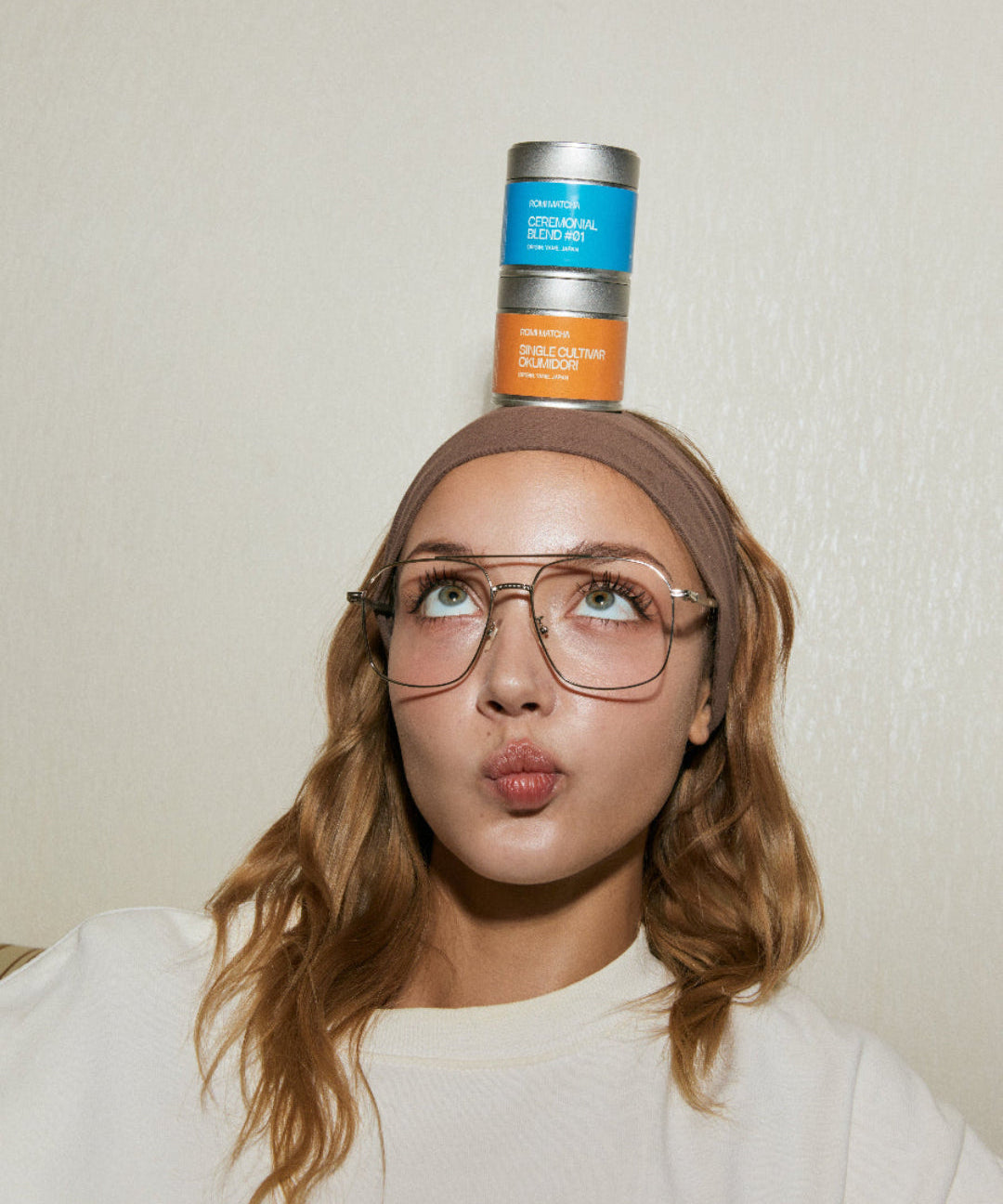 Person balancing matcha tins on their head with a neutral background
