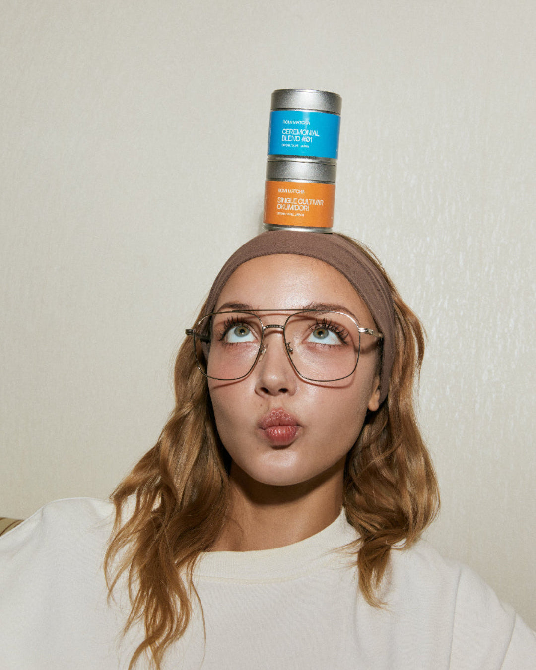 Person balancing matcha tins on their head with a neutral background