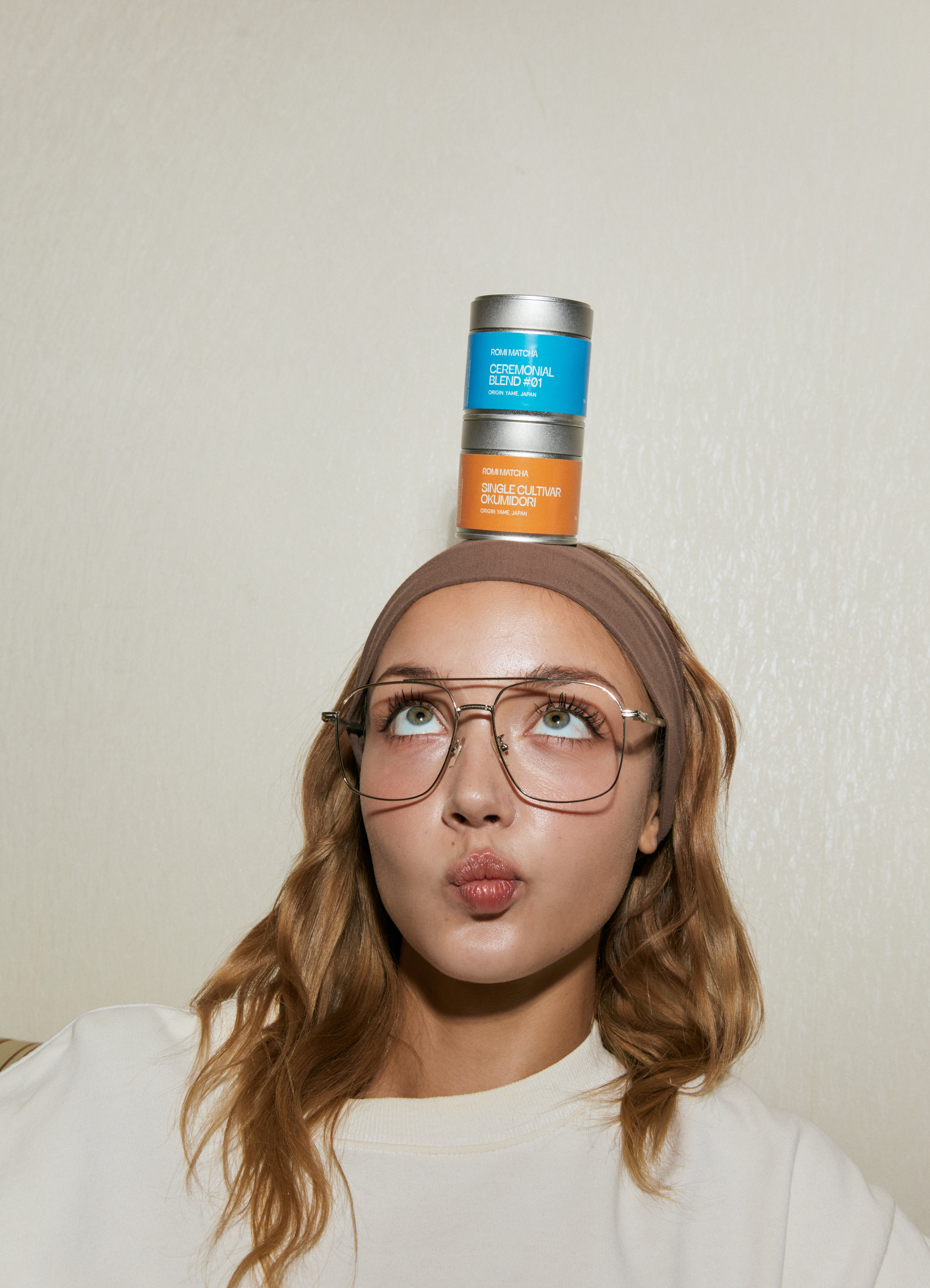 Person balancing matcha tins on their head with a neutral background